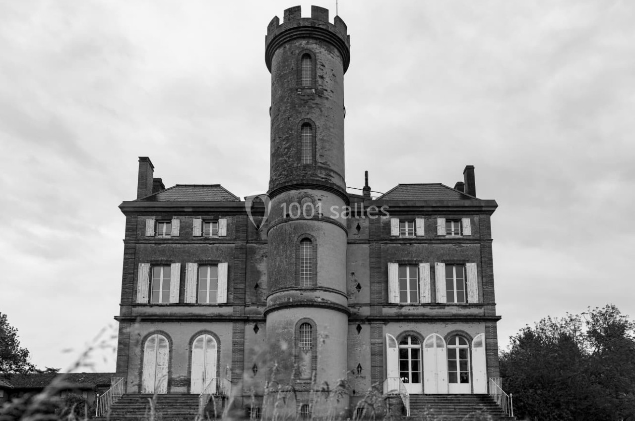 Façade d'un château ancien en pierre avec une tour centrale, photographié sous un ciel nuageux.