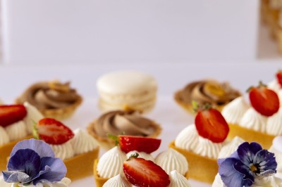 Tente blanche montée sur une pelouse, entourée de personnes et de tables, dans une cour avec bâtiments en arrière-plan.