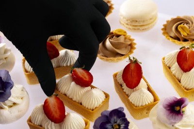 Tente blanche montée sur une pelouse, entourée de personnes et de tables, dans une cour avec bâtiments en arrière-plan.