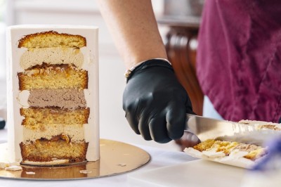 Tente blanche montée sur une pelouse, entourée de personnes et de tables, dans une cour avec bâtiments en arrière-plan.