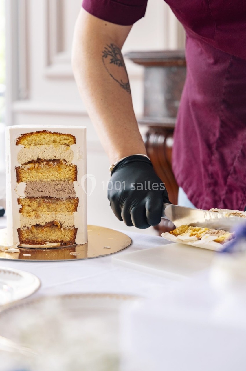 Une personne découpe une part de gâteau à étages avec un couteau, sur une table blanche.