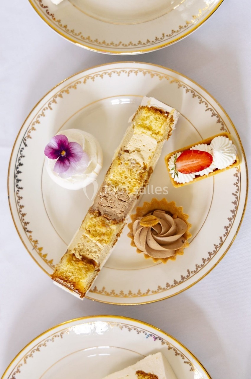 Assortiment de desserts sur une assiette en porcelaine, comprenant gâteau, tartelette, mousse et décoration florale.