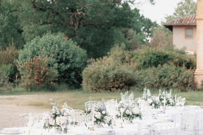 Tente blanche montée sur une pelouse, entourée de personnes et de tables, dans une cour avec bâtiments en arrière-plan.