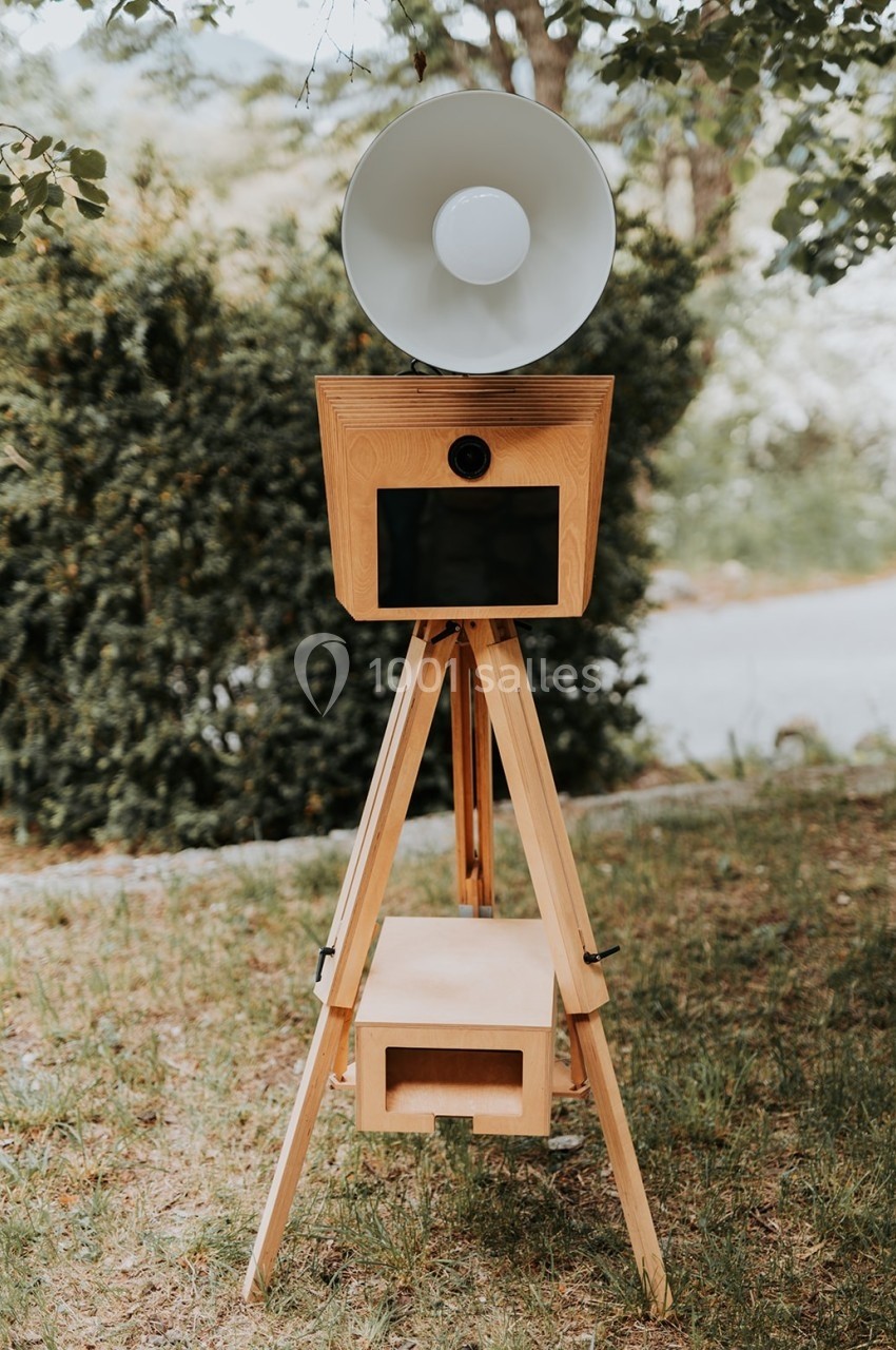 Appareil photo vintage sur trépied en bois avec lampe circulaire, installé en extérieur sur une pelouse.