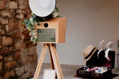 Appareil photo sur trépied en bois avec lampe circulaire, installé dans un jardin verdoyant.