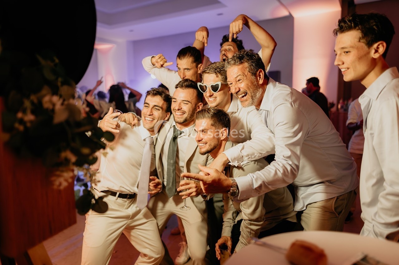 Un groupe d'hommes en tenue formelle pose joyeusement pour une photo lors d'un événement festif en intérieur.