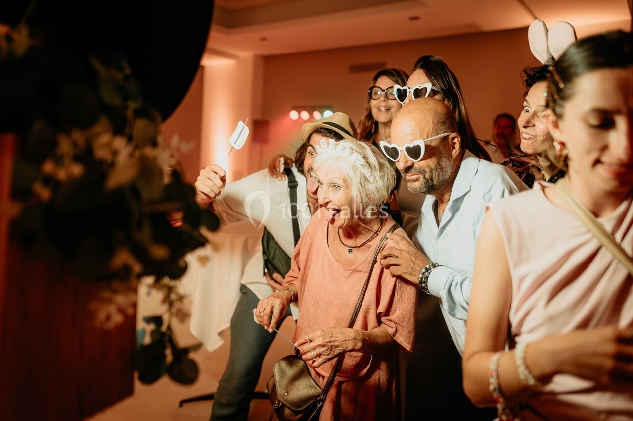 Des personnes souriantes posent ensemble dans un photobooth, portant des accessoires festifs comme des lunettes et des serre…