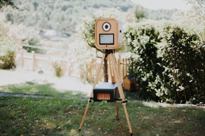 Appareil photo en bois monté sur un trépied, installé dans un jardin avec des arbres en arrière-plan.