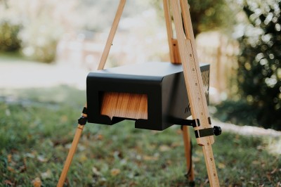 Appareil photo en bois monté sur un trépied, installé dans un jardin avec des arbres en arrière-plan.