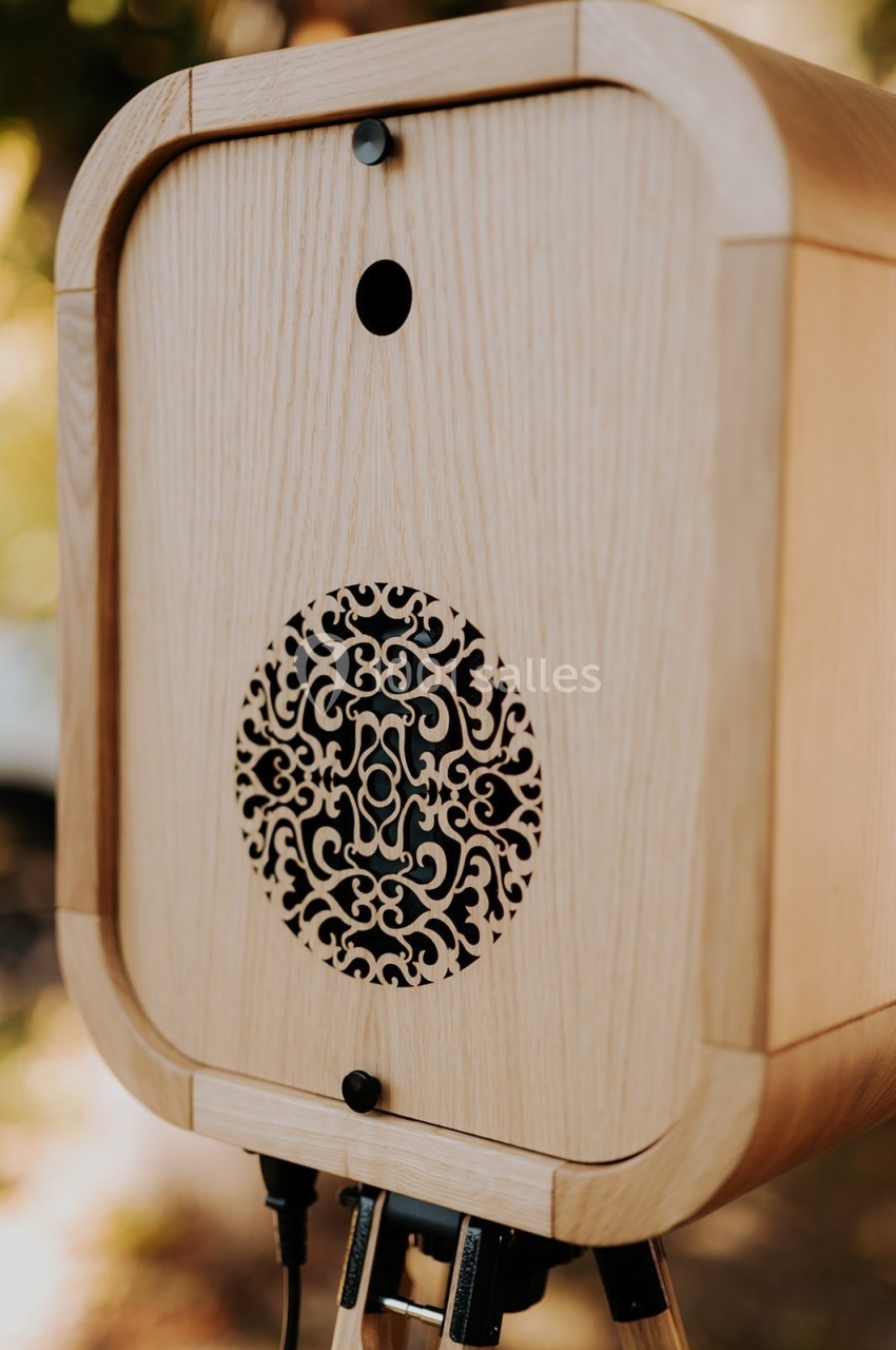 Boîtier en bois clair avec un motif décoratif circulaire ajouré, monté sur un trépied.