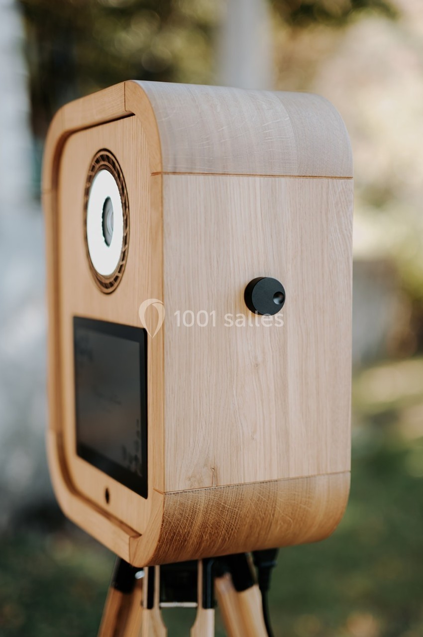 Boîtier en bois sur trépied avec un objectif circulaire et un écran intégré, placé en extérieur.