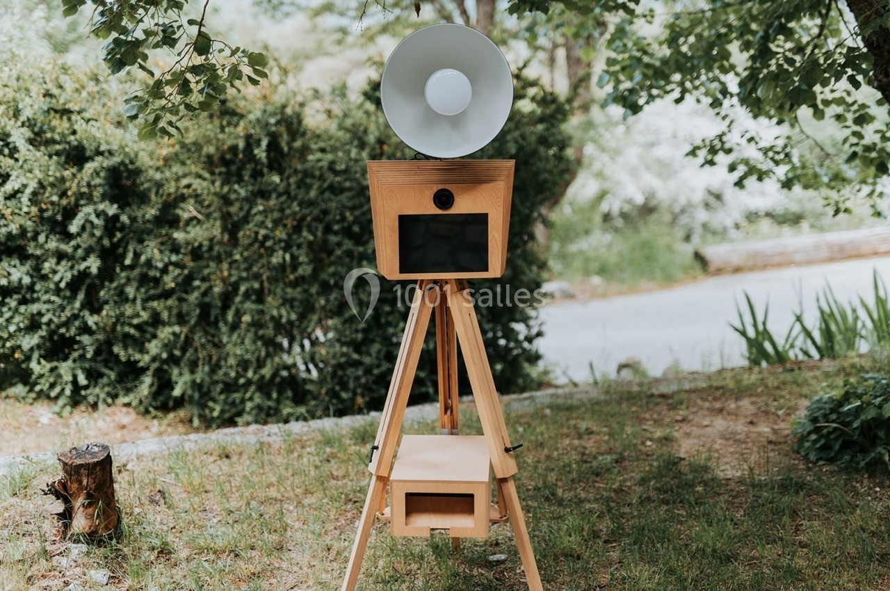 Appareil photo vintage sur trépied en bois, installé dans un jardin verdoyant.