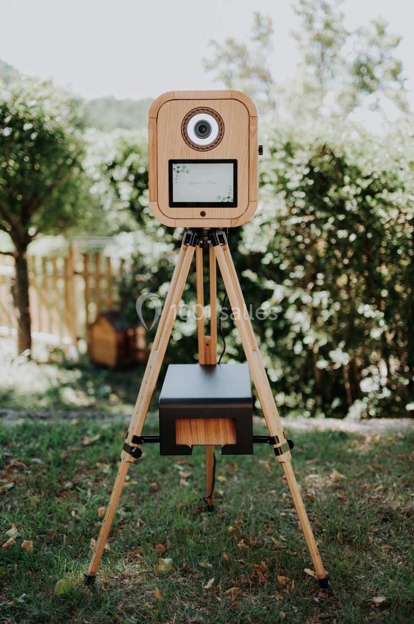 Appareil photo en bois sur trépied installé dans un jardin, entouré de végétation et de lumière naturelle.