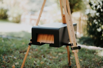 Boîtier en bois sur trépied avec un écran et un objectif circulaire, utilisé en extérieur.