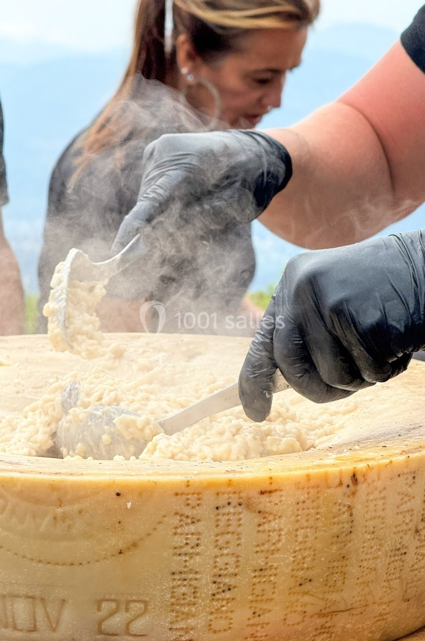 Préparation de risotto dans une meule de fromage, avec des mains gantées manipulant des ustensiles.