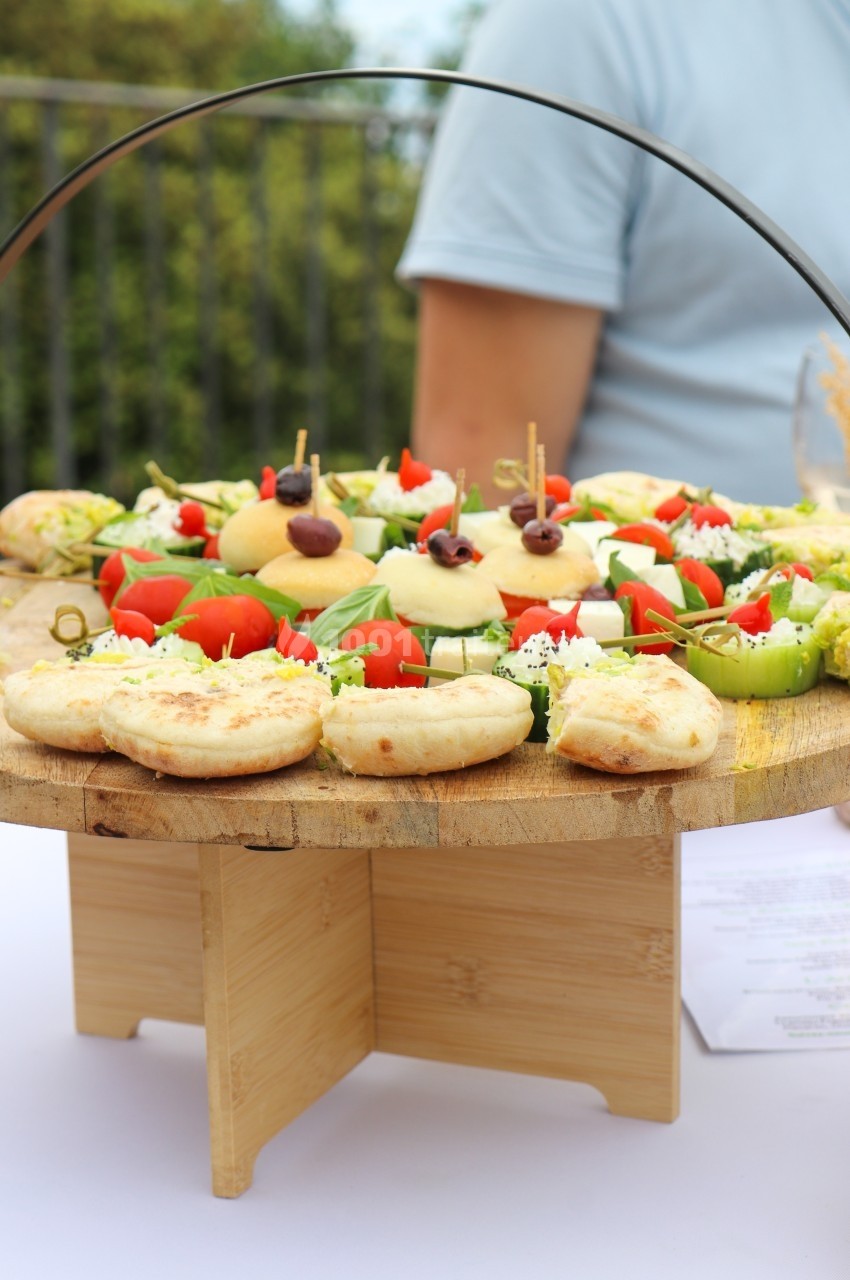Plateau en bois garni de mini-pizzas, légumes frais et amuse-bouches, présenté sur une table en extérieur.