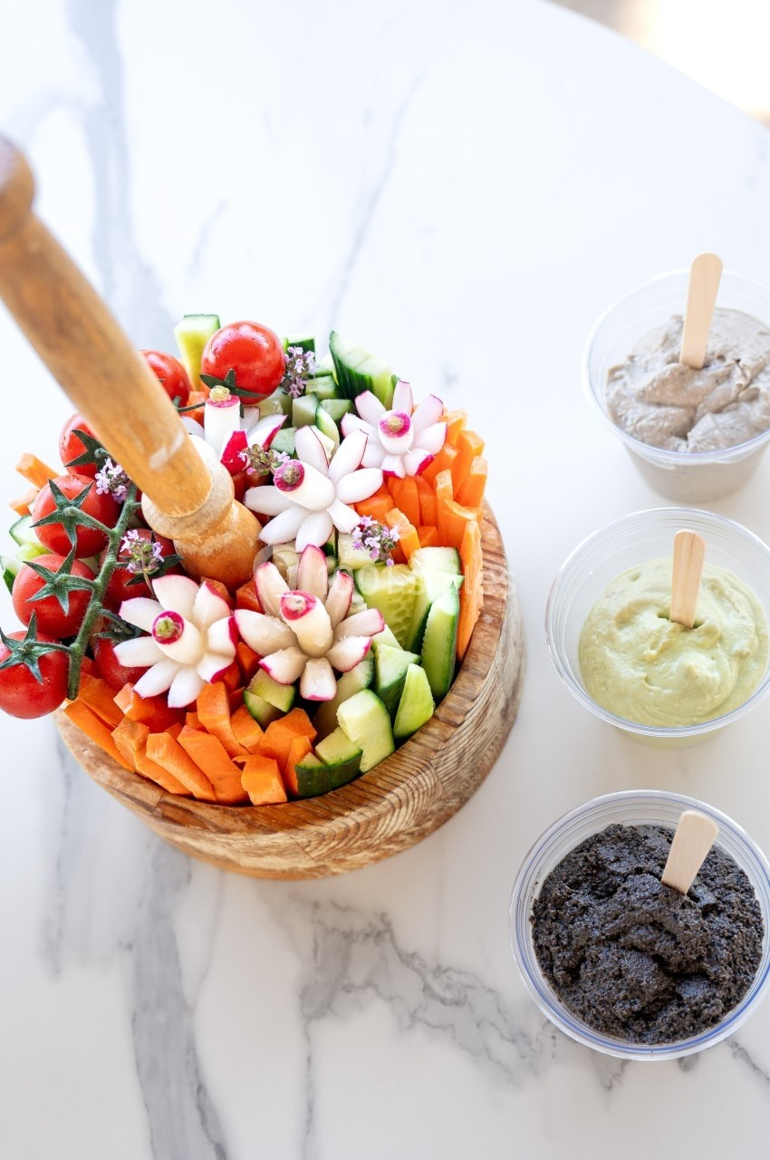 Assiette de crudités colorées avec carottes, concombres et radis, accompagnée de trois sauces dans des pots.