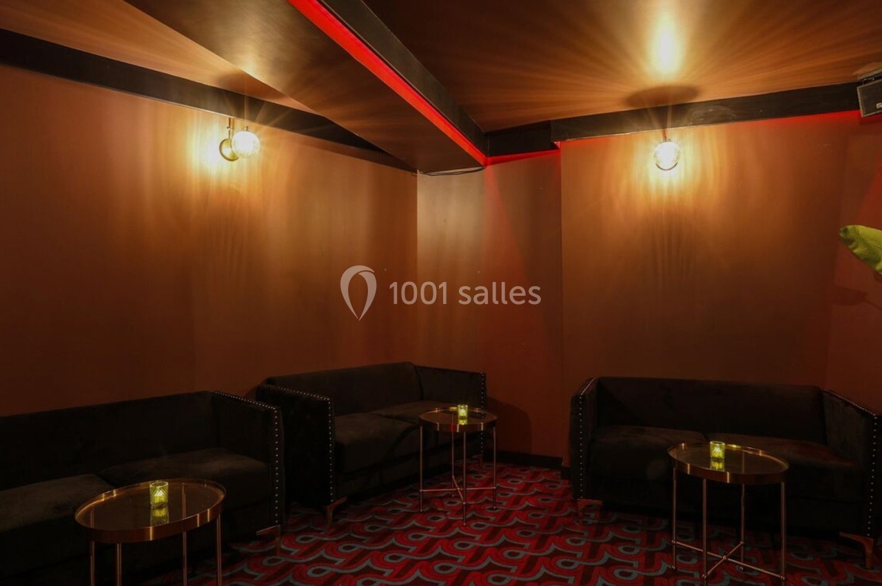 Salle au décor chaleureux avec murs marron, canapés noirs, tables basses dorées et éclairage tamisé.