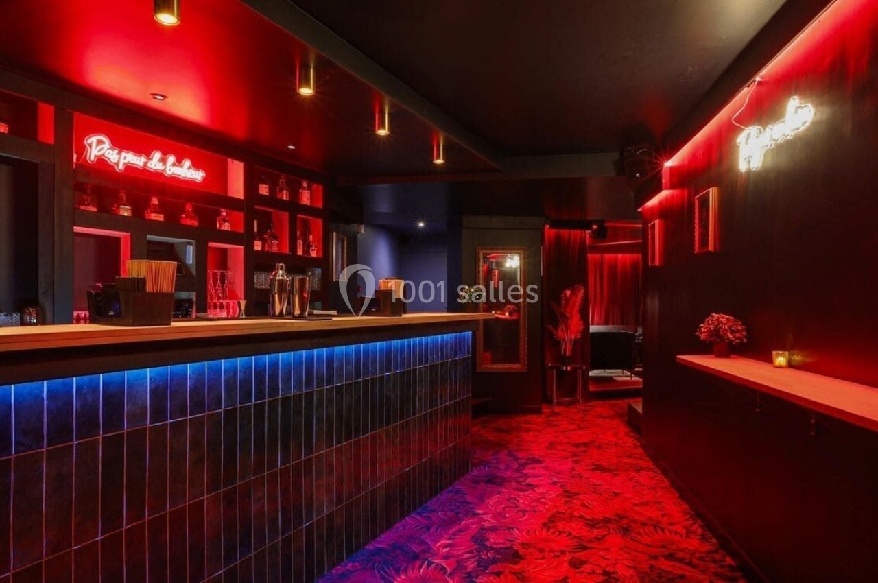 Bar moderne avec éclairage rouge et bleu, comptoir en bois, étagères avec bouteilles et ambiance tamisée.