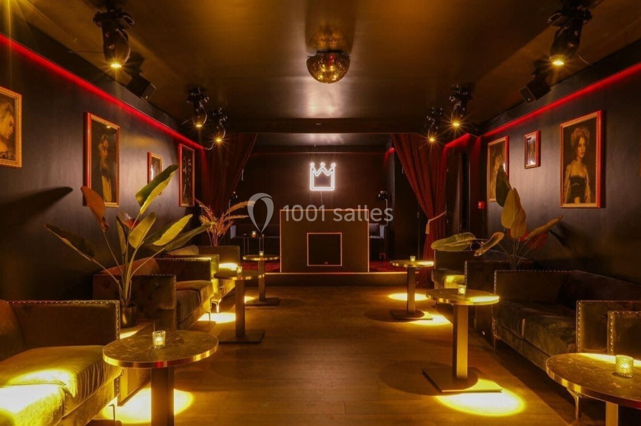 Salle de réception sombre avec éclairage tamisé, tables dorées, canapés et décoration murale artistique.
