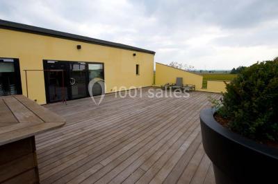 Piscine extérieure entourée de terrasses en bois et de chaises longues, devant une maison moderne sous un ciel dégagé.