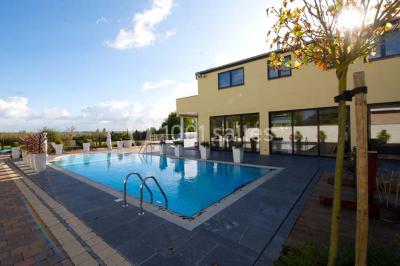 Piscine extérieure entourée de terrasses en bois et de chaises longues, devant une maison moderne sous un ciel dégagé.