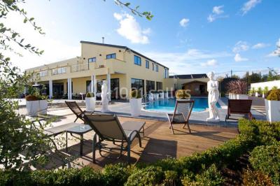 Piscine extérieure entourée de terrasses en bois et de chaises longues, devant une maison moderne sous un ciel dégagé.