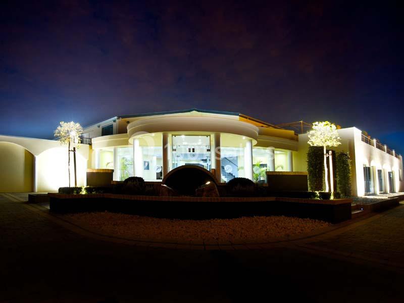 Façade d'une maison moderne éclairée la nuit, avec des arbres illuminés et une allée en pavés.
