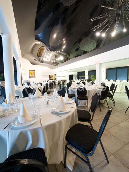 Salle de réception élégante avec tables rondes dressées, nappes blanches et chaises noires sous un plafond moderne.
