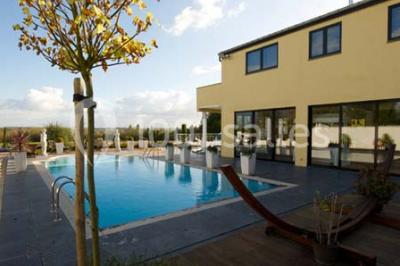 Piscine extérieure entourée de terrasses en bois et de chaises longues, devant une maison moderne sous un ciel dégagé.