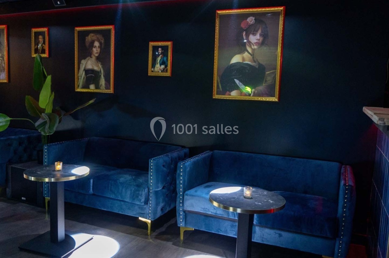 Canapés bleus et tables basses dans un intérieur sombre, décoré de portraits encadrés sur un mur noir.
