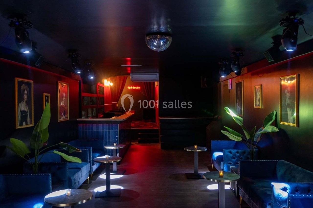 Intérieur d'un bar lounge avec canapés bleus, tables basses, éclairage tamisé et décorations murales.