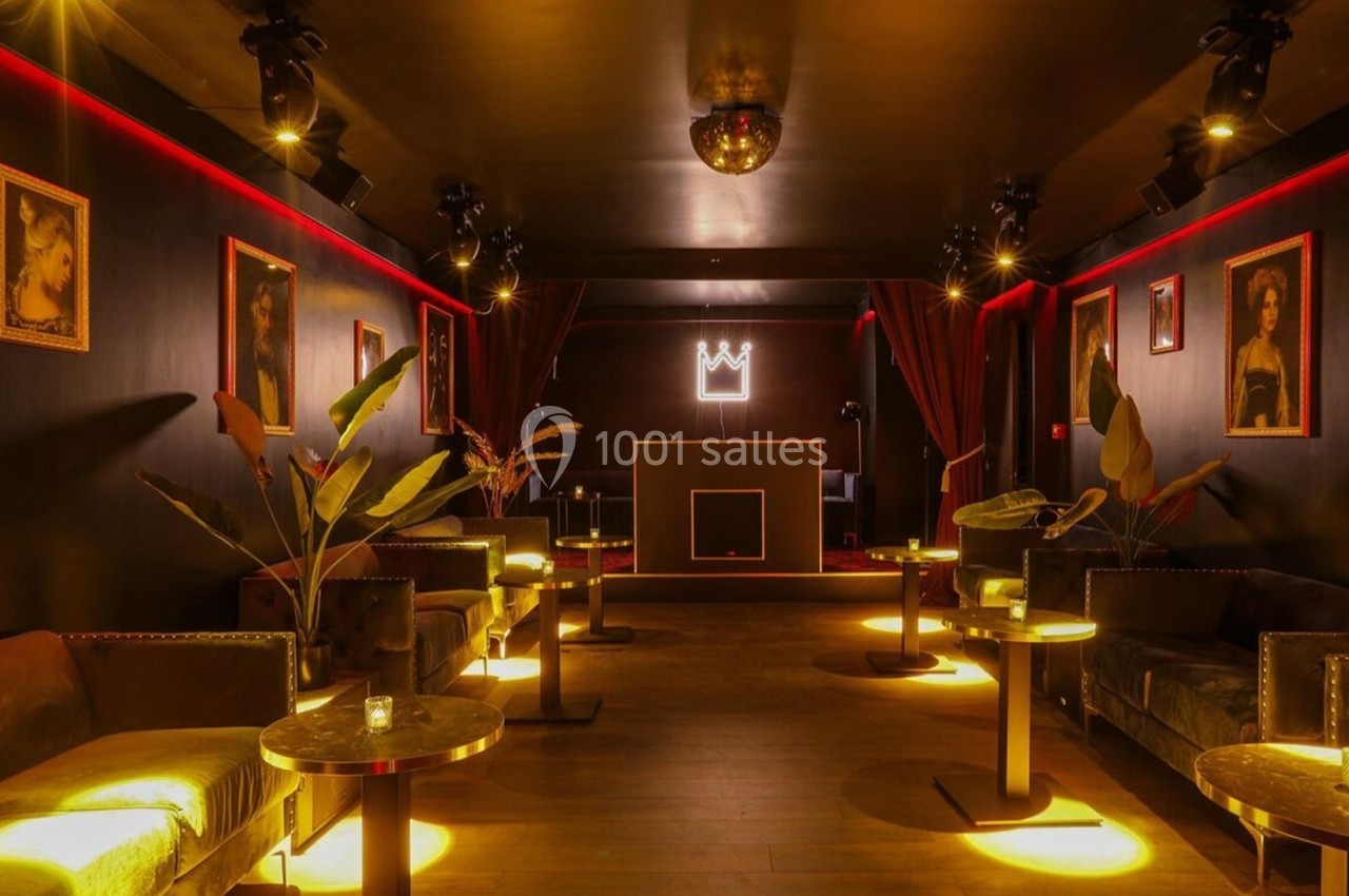 Salle lounge sombre avec canapés, tables basses, éclairage tamisé, décorations murales et une couronne lumineuse au fond.