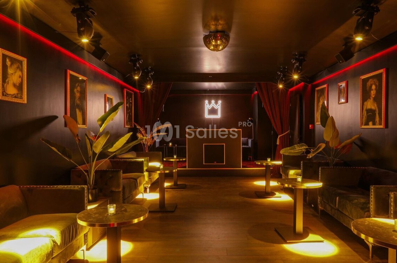 Salle lounge sombre avec canapés, tables basses, éclairage tamisé, décorations murales et une couronne lumineuse au fond.