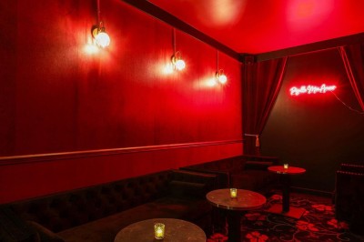 Façade d'un établissement avec une entrée vitrée, éclairée par une lumière rouge et une enseigne lumineuse bleue.