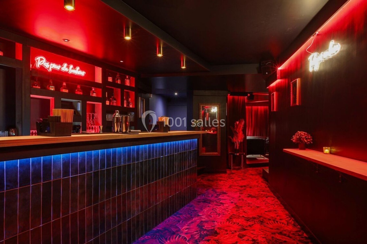 Bar à l'éclairage tamisé avec comptoir en bois, néons rouges et bleus, et décorations murales sombres.