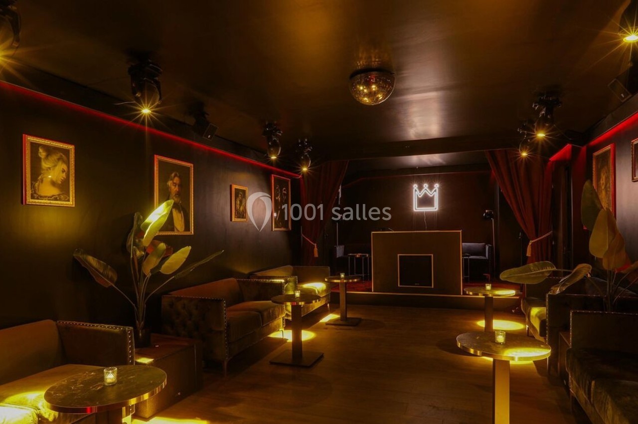 Salle sombre et élégante avec canapés, tables éclairées, portraits aux murs et une cabine de DJ au fond.