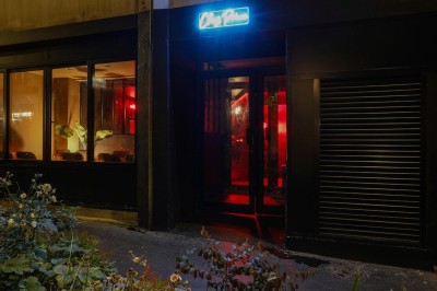 Façade d'un établissement avec une entrée vitrée, éclairée par une lumière rouge et une enseigne lumineuse bleue.