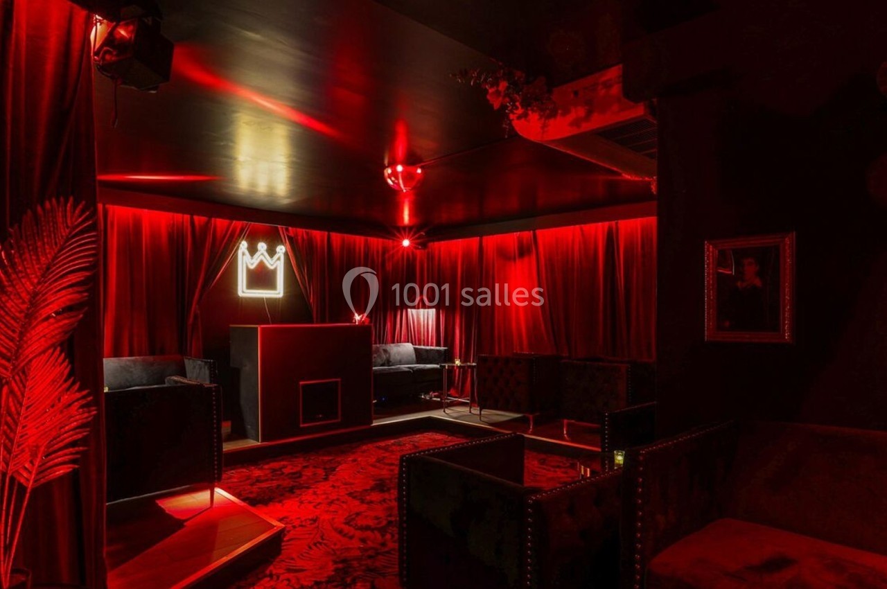 Salle lounge avec éclairage rouge tamisé, fauteuils sombres, rideaux en velours et décoration murale minimaliste.