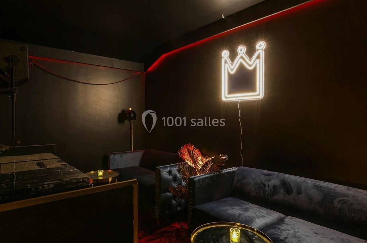 Salle sombre avec canapé, table basse, décoration lumineuse en forme de couronne et ambiance tamisée.