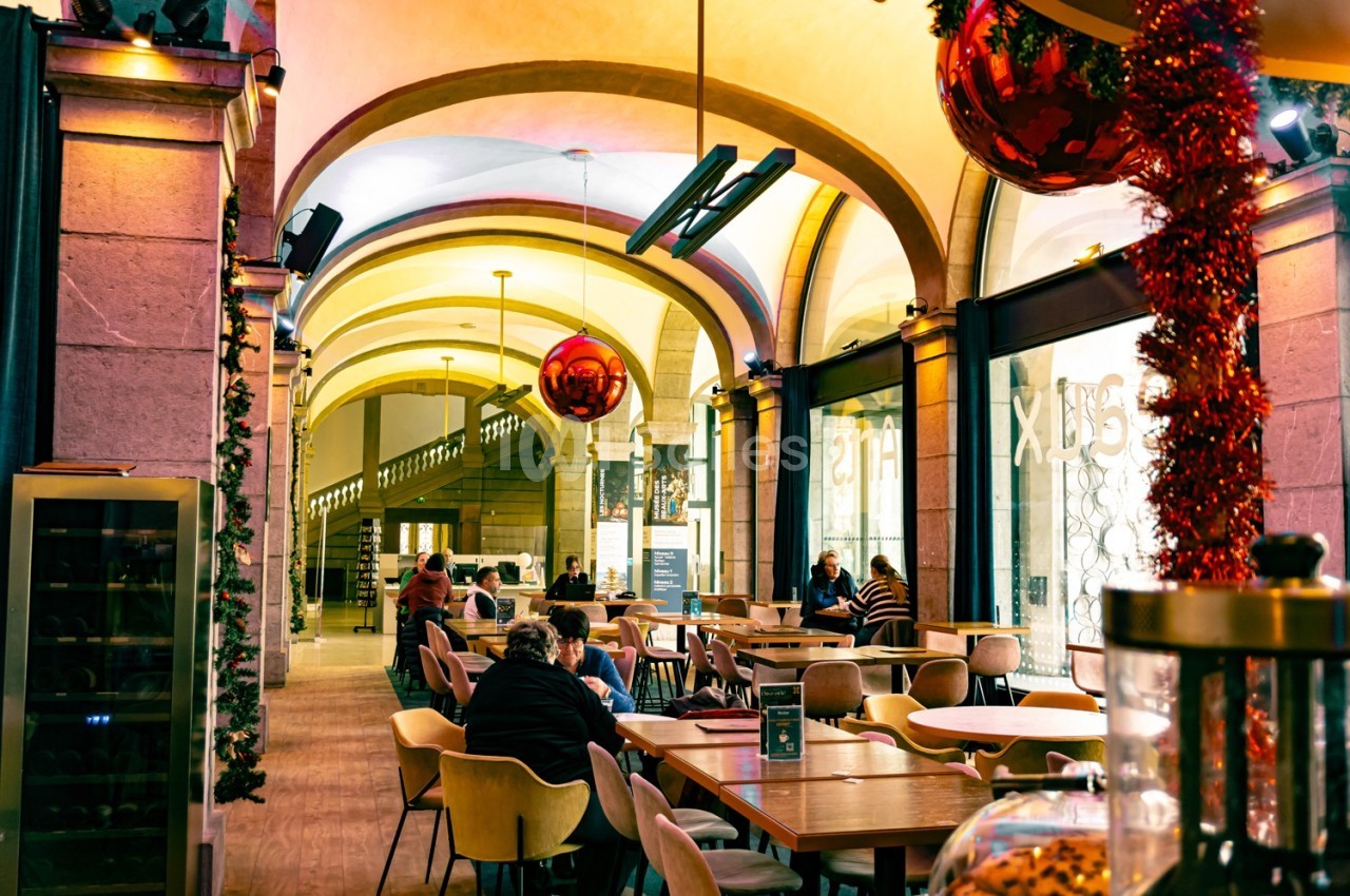 Salle de restaurant lumineuse avec des tables occupées, décorations de Noël suspendues et arches en pierre.