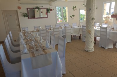 Salle de réception décorée avec des tables rondes dressées, nappes blanches et chaises ornées de nœuds rouges.