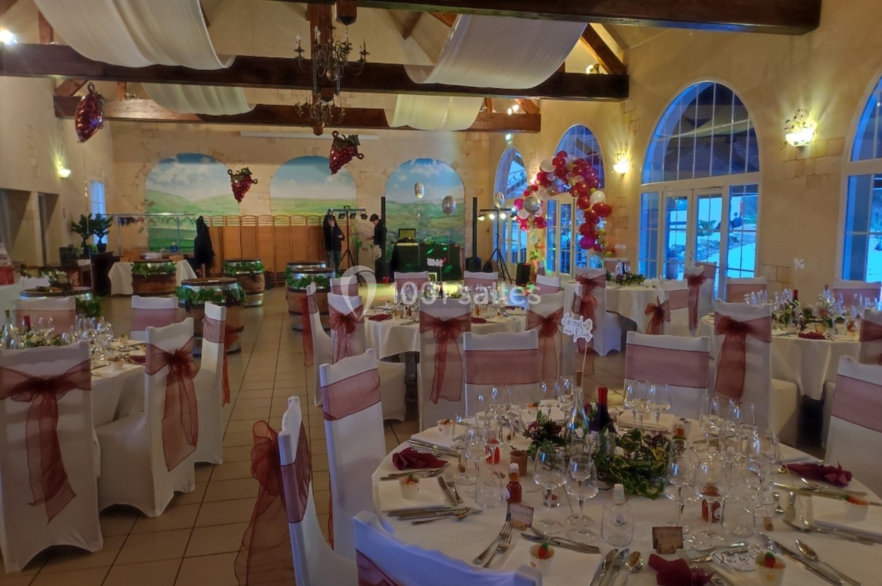 Salle de réception décorée avec des tables rondes dressées, nappes blanches et chaises ornées de nœuds rouges.