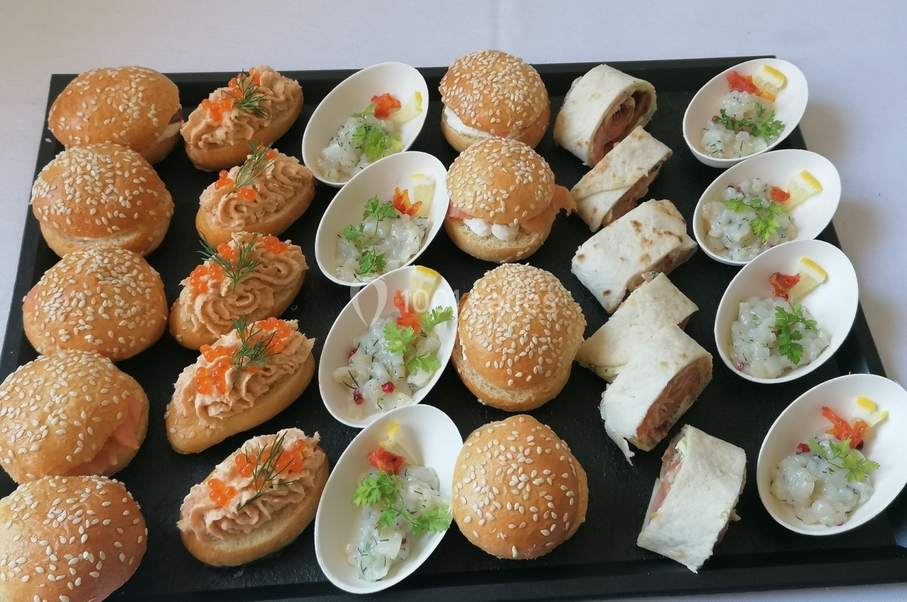 Plateau de bouchées apéritives variées comprenant mini-burgers, wraps et verrines sur une table blanche.