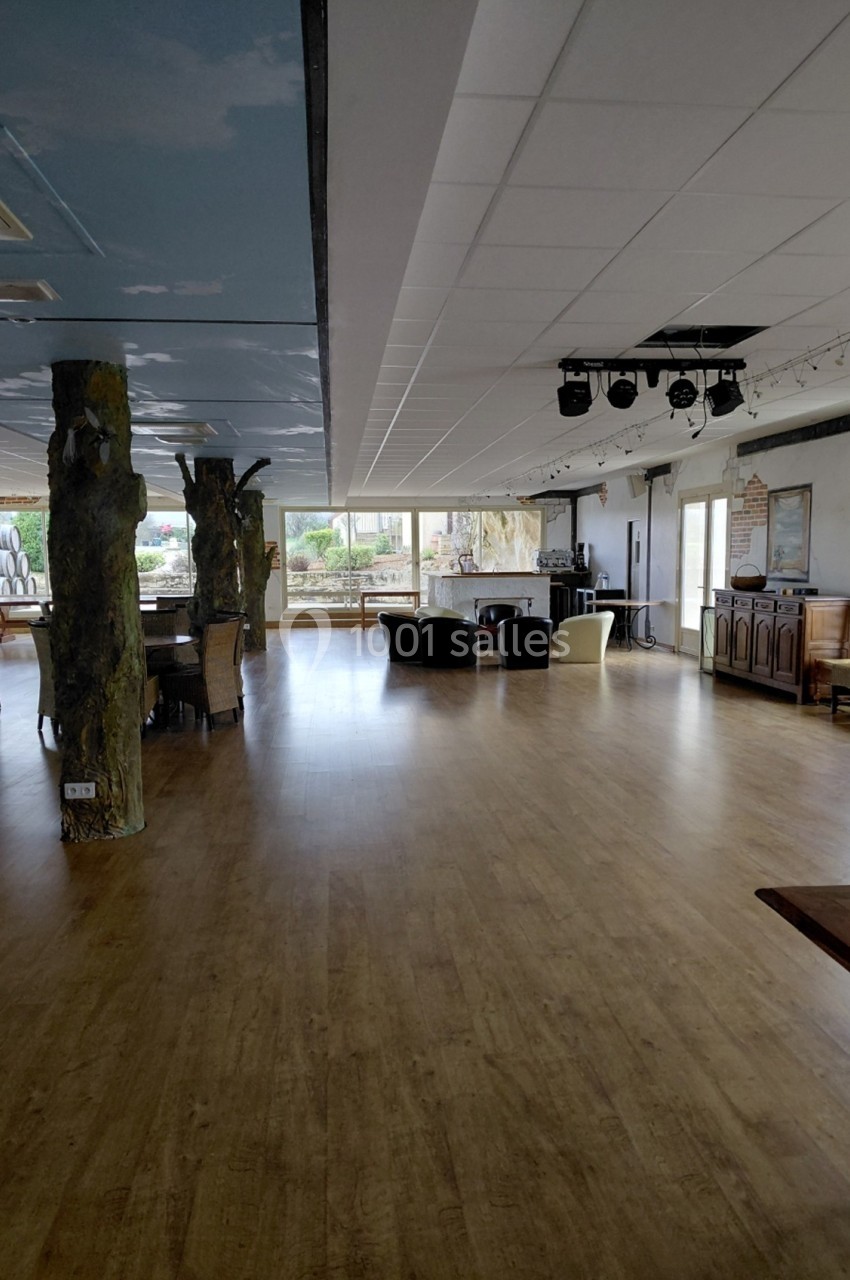 Salle spacieuse avec parquet, mobilier épars, colonnes décoratives et grandes fenêtres laissant entrer la lumière naturelle.