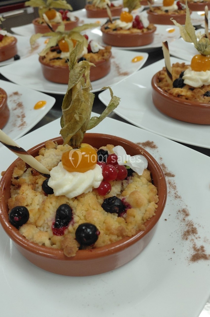 Desserts individuels en ramequins garnis de crumble, fruits rouges, physalis, crème et décoration en chocolat.