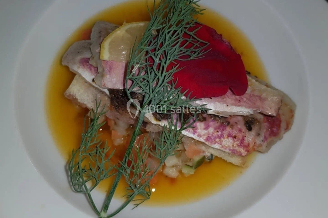 Plat de poisson dressé avec une sauce orange, garni d'aneth, d'une tranche de citron et d'une fleur rouge.