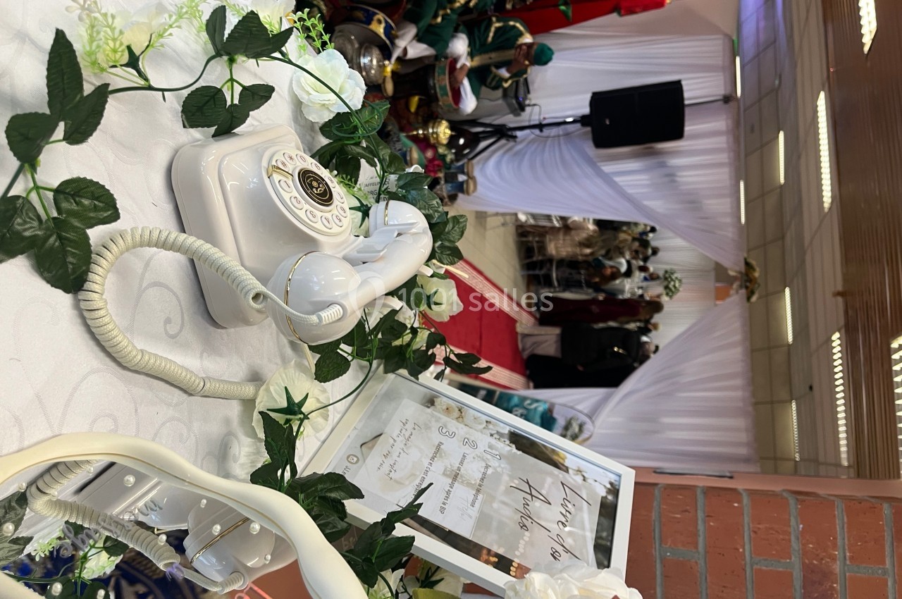 Téléphone rétro blanc décoré de fleurs sur une table lors d'un événement avec des invités en arrière-plan.