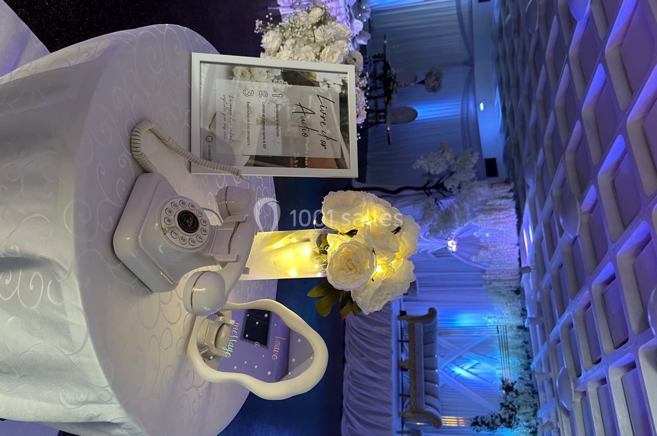 Téléphone vintage blanc sur une table décorée de fleurs et lumières, dans une salle de réception élégante.