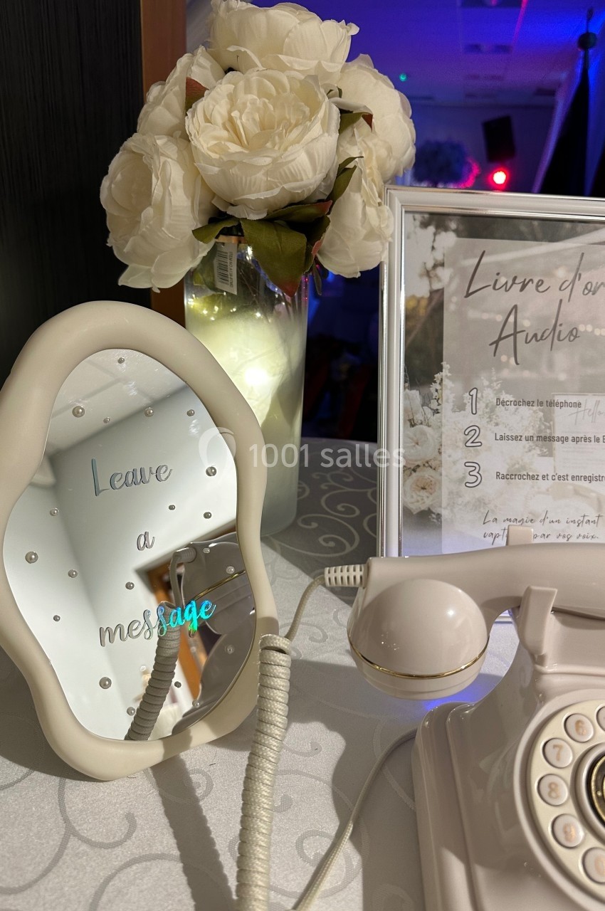 Téléphone vintage blanc posé sur une table avec un miroir indiquant ’Leave a message’ et un vase de fleurs blanches en…